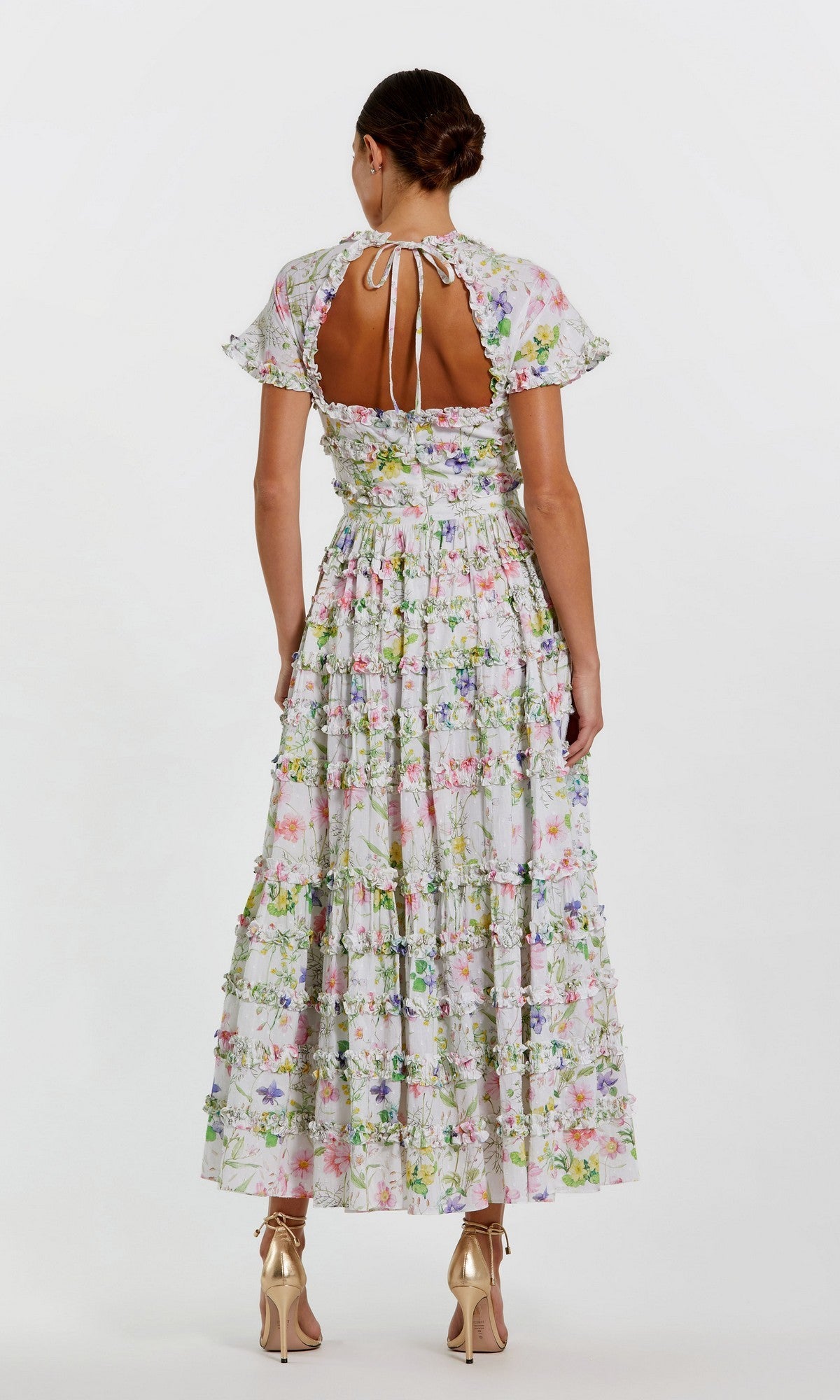 A woman stands facing away, wearing the Mac Duggal 8079 Midi Wedding Guest Dress with short sleeves, an open back, and a fit-and-flare silhouette, elegantly paired with gold high-heeled shoes.